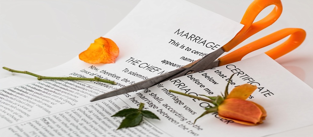 A pair of scissors cutting an orange flower placed on a paper labeled “Marriage Certificate.”