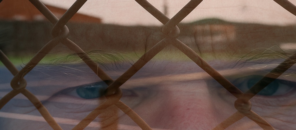 A translucent, worried man superimposed over barbed wire fencing, symbolizing the fear and uncertainty caused by the U.S. 2025 mass deportation policies.