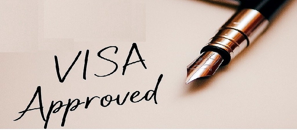 Dolma kalemle “Visa Approved” yazılmış ve üzerinde ABD Göçmenlik vize damgası bulunan bir kâğıdın yakın plan görüntüsü.