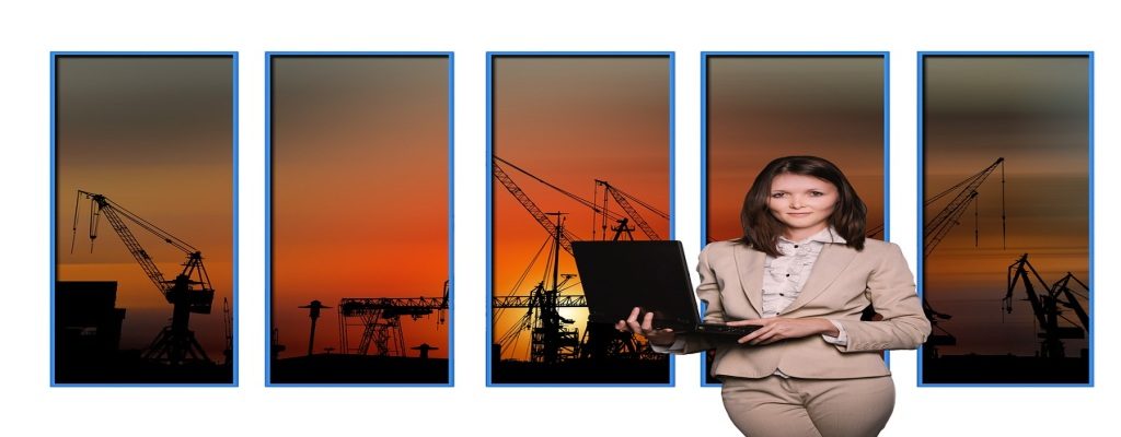 A confident businesswoman holding a laptop, standing in front of an industrial background at sunset — symbolizing employment-based Green Card eligibility
