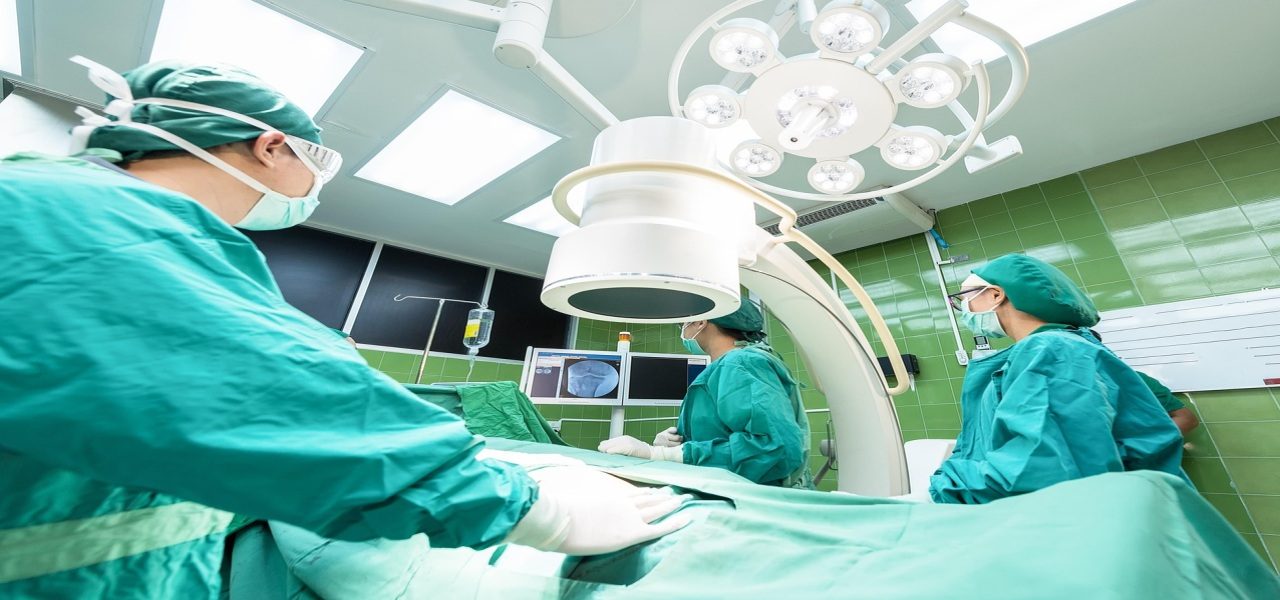 Surgeons in green gowns performing a procedure inside a fully equipped operating room.