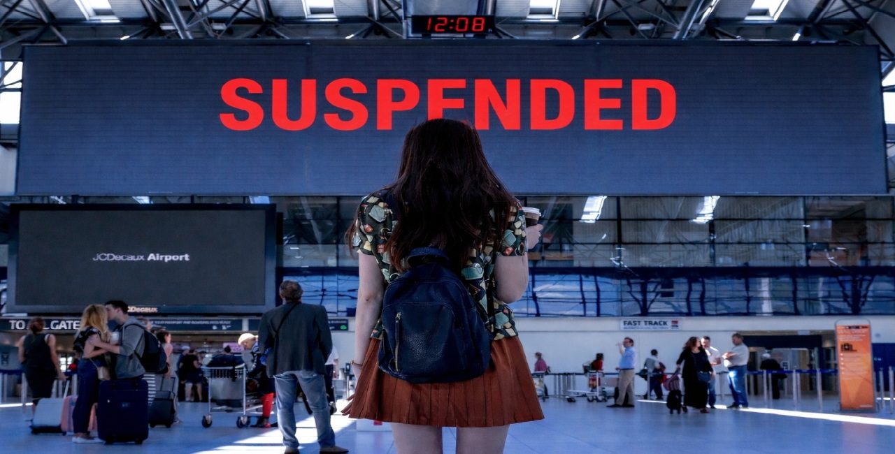 Traveler looking at an airport screen showing “SUSPENDED,” symbolizing immigrant visa processing restrictions.