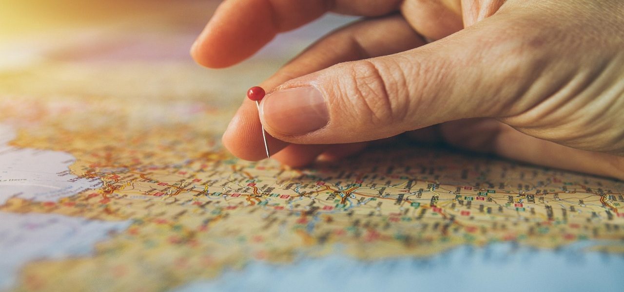 Una mano colocando un alfiler rojo sobre un mapa detallado.