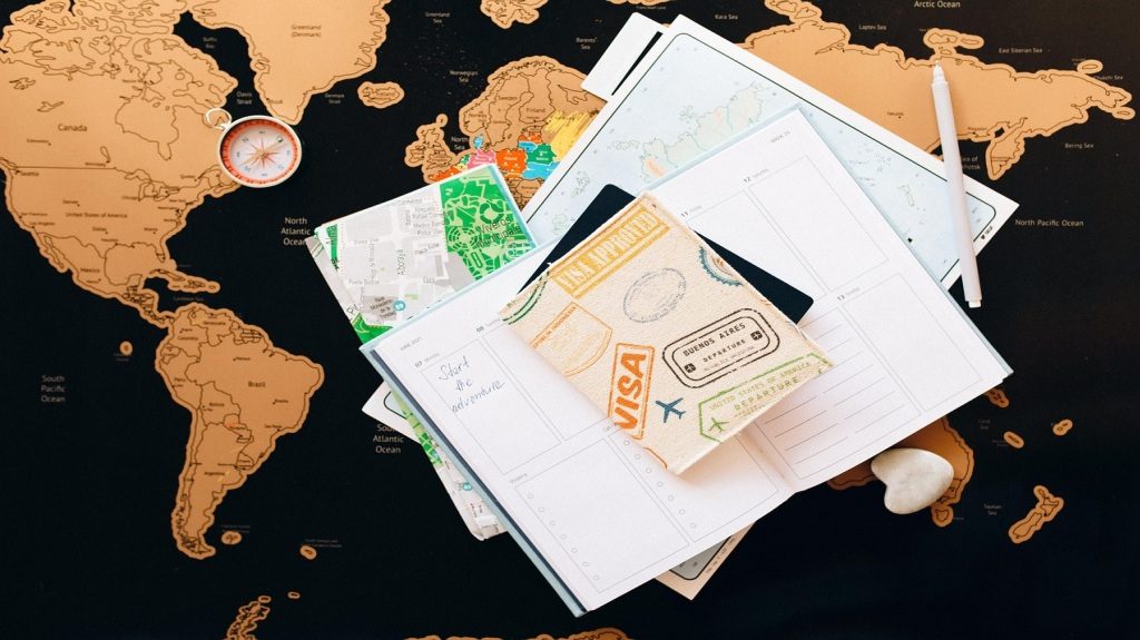 A visa document holder, compass, and travel papers placed on a world map.
