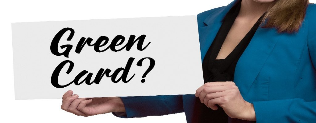 A woman holding a sign that reads “Green Card?”, with her face not visible